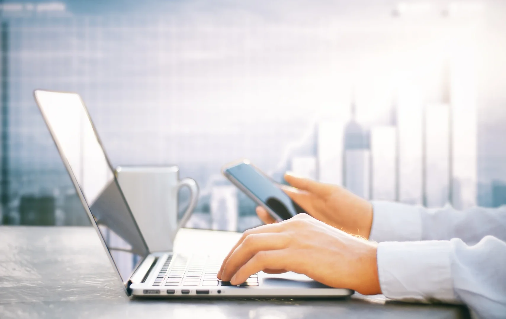 Delineante en su oficina de trabajo consultando su móvil y ordenador portatil