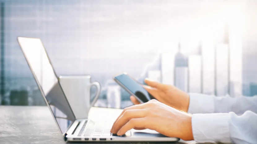 Delineante en su oficina de trabajo consultando su móvil y ordenador portatil