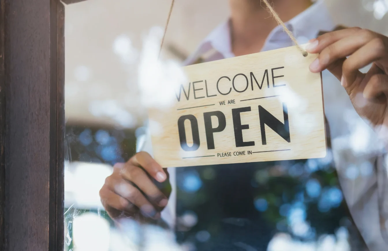 Empleado de un comercio sujetando el típico letrero que suele encontrarse en la puerta y que indica que el local está abierto