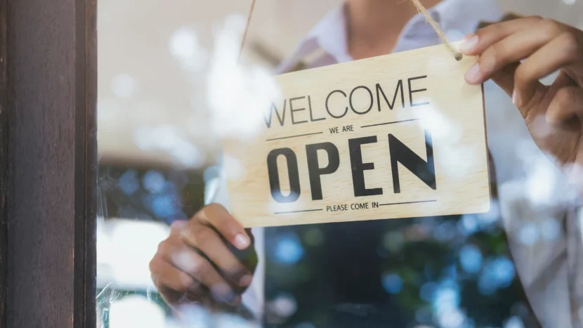 Empleado de un comercio sujetando el típico letrero que suele encontrarse en la puerta y que indica que el local está abierto